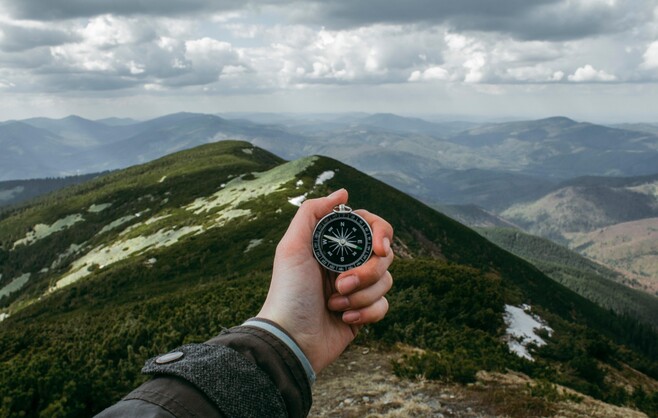 hand holding compass in front of mountains