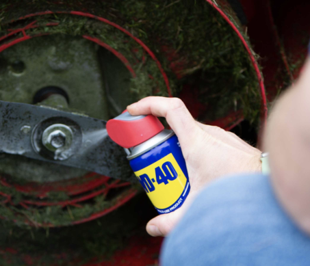 man applying WD-40 project to lawnmower